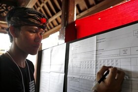Uomo sotto una tettoia in legno segna -a mano, su carta, con un trattino e una diagonale ogni 5- i voti ricevuti dai candidati