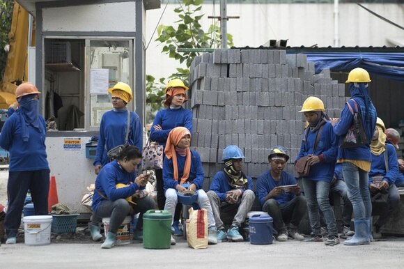 Migranti cambogiani che lavorano nell edilizia riuniti davanti a un edificio e a una pila di mattoni.