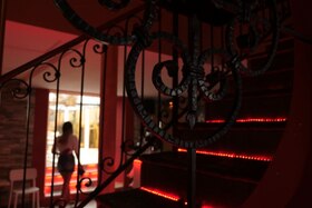Una donna vista di schiena in un locale in penombra con luci rosse sulle scale in primo piano