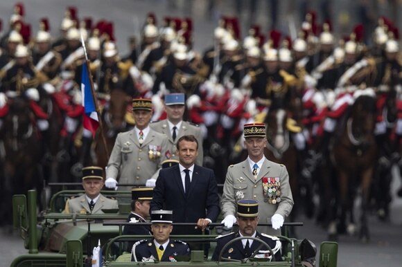 Macron su un veicolo militare durante la parata con accanto diversi militi super decorati