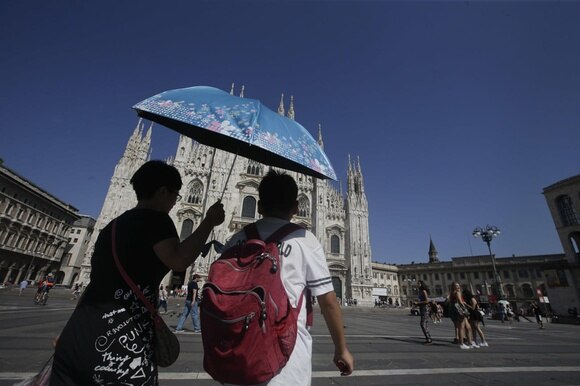 Due persone si riparano dal sole con un ombrello davanti al Duomo di Milano