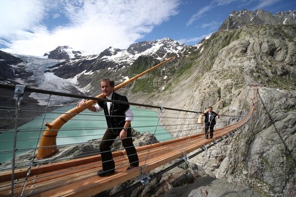 due uomini con dei corni delle alpi su un ponte sospeso in montagna