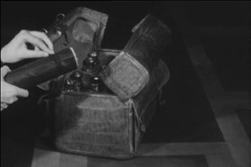Bauletto di cuoio contenente bottiglie e boccette; mani stanno per inserire un cilindro portadocumenti