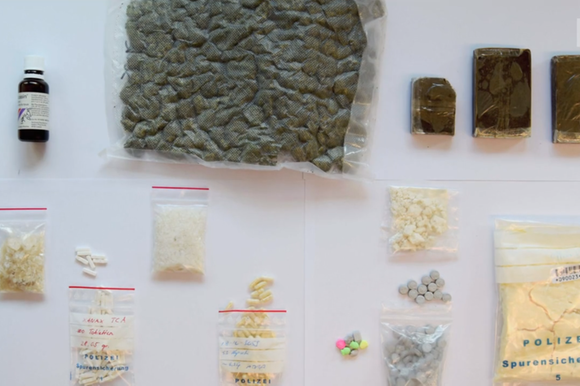 Vista dall alto di confezioni/boccette/buste di droghe e farmaci posate ordinatamente su un tavolo bianco