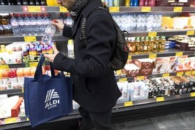 Giovane con zainetto e sacchetto in tessuto davanti a un frigo di un supermercato ripone una bottiglietta d acqua