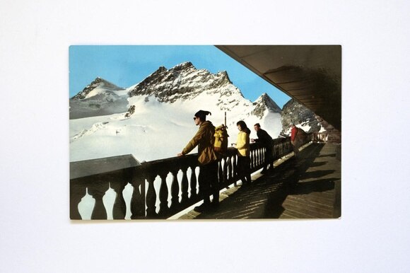 Fotografia di una cartolina che ritrae escursionisti di montagna che ammirano un paesaggio alpino da una terrazza.