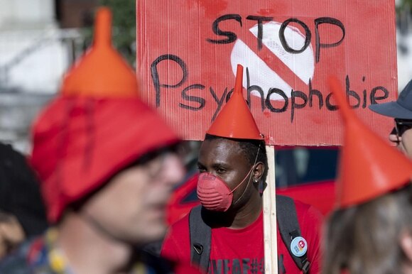 Persone manifestano con un imbuto in testa a mo di cappello e cartello Stop psychophobie