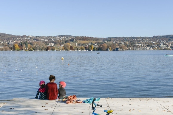 A woman and two young children sit on the waterfront of Lake Zurich