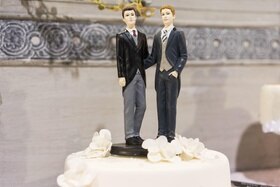 Una statuetta che reappresenta una coppia di uomini su una torta nuziale.