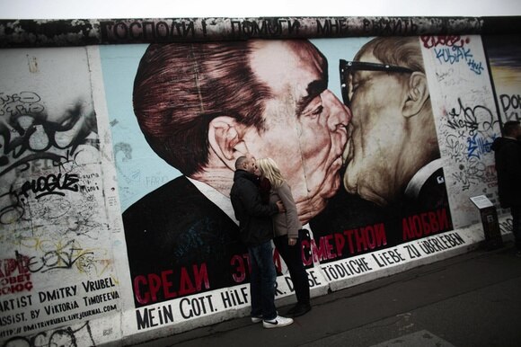 Una coppia si bacia davanti al dipinto sul muro di Berlino che ritrae il bacio di Brezhnev con Honecker.