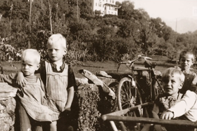 Foto in bianco e nero di quattro bambini con grembiulino vicini a un muretto in paesaggio di campagna