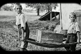 Due bambini trasportano una cassa nei pressi di una fattoria.