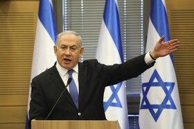 Beyamin Netanyahu a un pulpito fa un gesto col braccio sinistro; dietro, bandiere israeliane