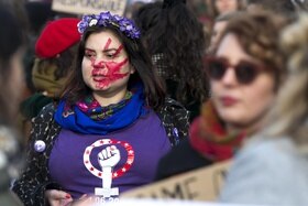 Gruppo di donne; a fuoco, una che indossa la maglia dello sciopero delle donne e con impronta di mano dipinta sul volto