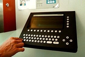 Primissimo piano di un dispositivo elettronico con tastiera alfanumerica e schermo applicato su parete di cabina telefonica