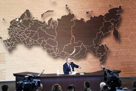 Vladimir Putin seduto al tavolo di una grande sala stampa; dietro di lui, enorme cartina muta della Federazione russa
