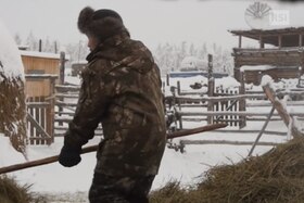 Un uomo sposta del fieno in una fattoria dove tutto è coperto da una coltre di neve