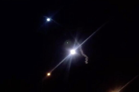 Due bagliori con una scia di fumo appena visibile in un cielo completamente buio, notturno