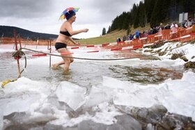 Una donna in costume da bagno e con ombrellino sulla testa esce da un lago alpino parzialmente ghiacciato