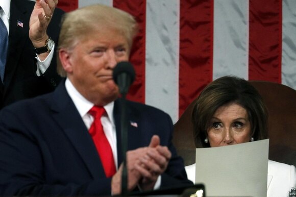 Mezzo busto di Trump che sorride e applaude, sfuocato; dietro, a fuoco, Nancy Pelosi guarda perplessa semi-coperta da un foglio