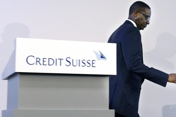 Uomo di colore, in abito formale, si allontana da un pulpito con la scritta Credit Suisse