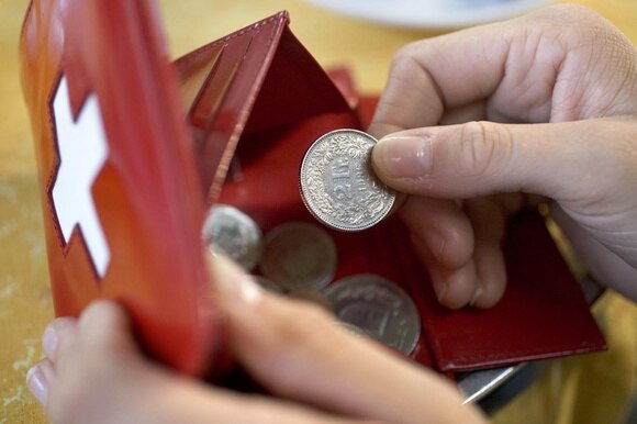 Un portamonete con la bandiera svizzera e una mano che coglie una moneta da due franchi.