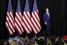 Pete Buttigieg in un comizio a Des Moines in Iowa: sul palco con 4 bandiere americane alle spalle.