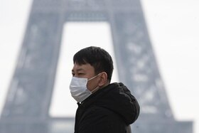 Un turista asiatico con la mascherina ai piedi della Tour Eiffel di Parigi