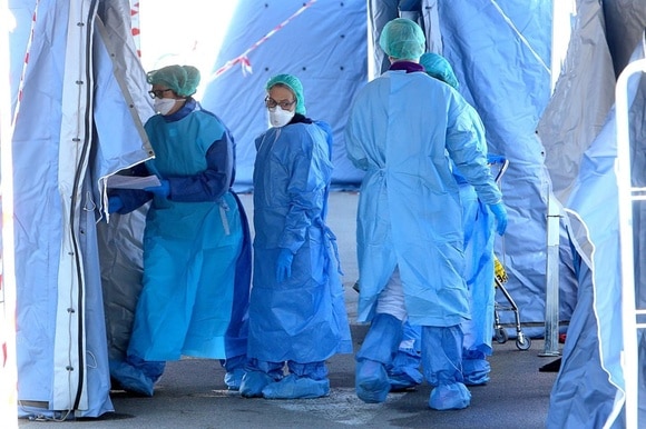 Persone con camice azzurro sotto quella che sembra la tenda di un ospedale da campo