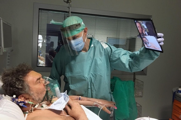 Man holds tablet for patient to talk to his relatives from hospital
