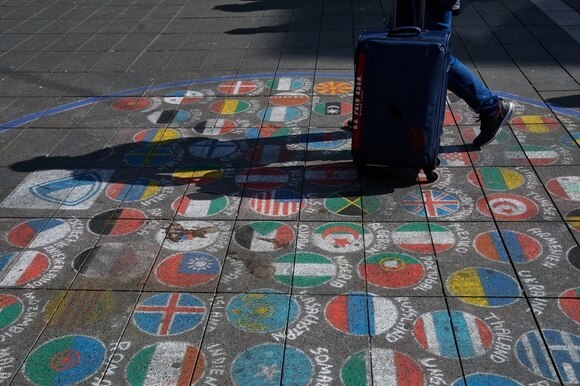 Ein Mann schiebt seinen Koffer über Flaggen verschiedenster Länder, die mit Kreide auf den Boden der Fußgängerzone gemalt wurden