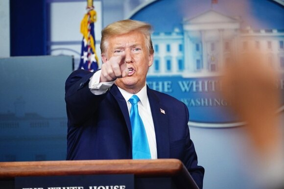 Trump indica qualcuno con l indice (forse un giornalista cui dà parola) da un pulpito; dietro di lui stemma della Casa Bianca