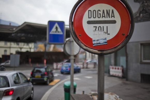 Primo piano di cartella Dogana-Zoll ; dietro, sfuocare, automobili passano sotto una grossa struttura aperta