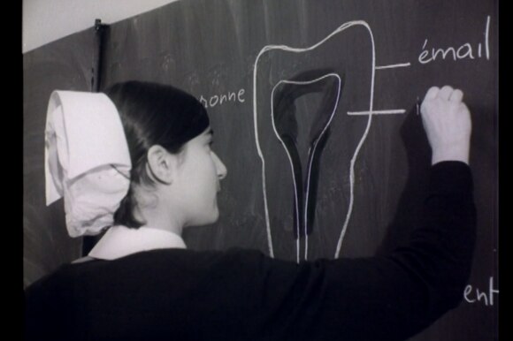 Giovane donna con copricapo da infermiera di quelli che si usavano un tempo disegna alla lavagna schema di un dente