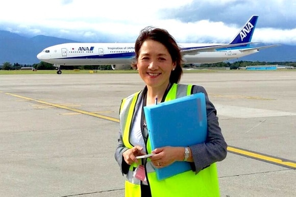 Una donna sorridente su una pista di un aeroporto e sullo sfondo un aereo.