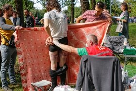 Uomo di schiena mostra lividi sulle gambe; un paramedico lo aiuta; altre due persone coprono con un telo