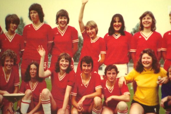 Squadra di calcio femminile con casacca rossa in foto di gruppo nella tipica posizione delle squadre di calcio