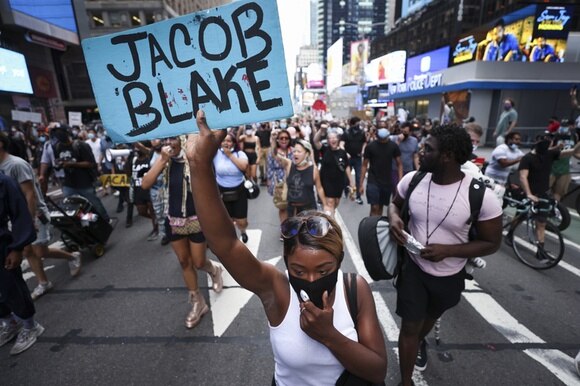 Donna di colore guida un corteo con cartello con scritto Jacob Blake su una strada di città