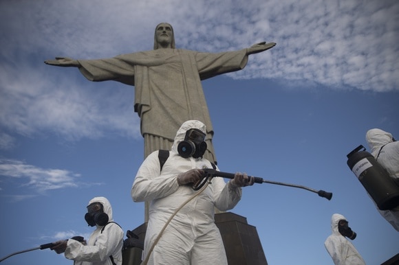 Davanti al simbolo di Rio de Janiero diversi persone maschere e tute disinfettano la zona.