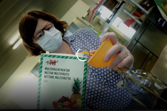 Donna con mascherina travasa del succo multifrutta da un tetrapack a una bottiglia in un laboratorio