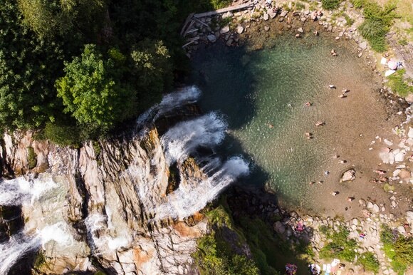 Immagine aerea di cascate di montagna con pozza e gente che fa il bagno