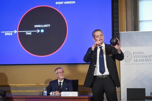 Un membro dell accademia delle scienze svedesi spiega alla stampa la scoperta del buco nero.