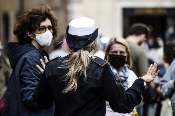 Un agente di polizia e due passanti in luogo aperto affollato, indossano tutte mascherina