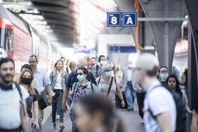 Persone si muovono lungo la banchina di una stazione ferroviaria che dalla segnaletica si riconosce come svizzera