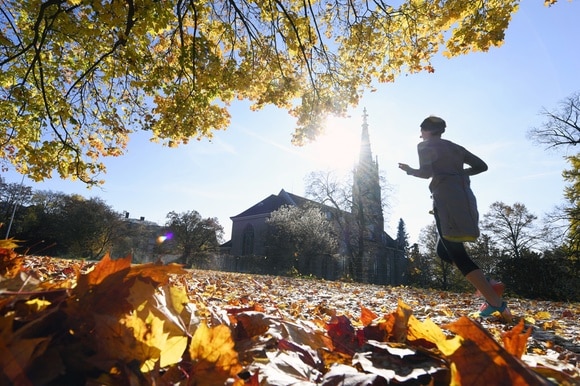 Donna fa jogging su un prato colmo di foglie secche davanti a una chiesetta in giornata soleggiata