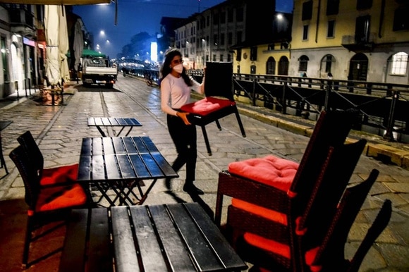 Esercente lungo un naviglio a Milano dispone o raccoglie sedie e tavolini dallo spazio esterno al bar