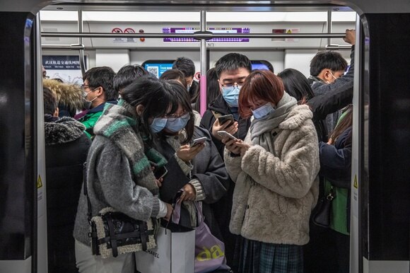 Vagone di metropolitana con porte aperte, passeggeri con mascherina controllano il proprio smartphone