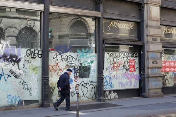 Un anziano signore cammina in centro di Milano davanti a negozi chiusi per fallimento.