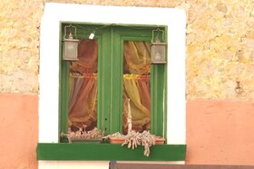 Casa con pareti gialle e rosse; primo piano di finestra con infissi e davanzale verdi, cornice bianca; tendine