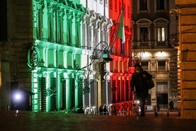 Palazzo Chigi illuminato col tricolore di sera, visto da piazza Montecitorio